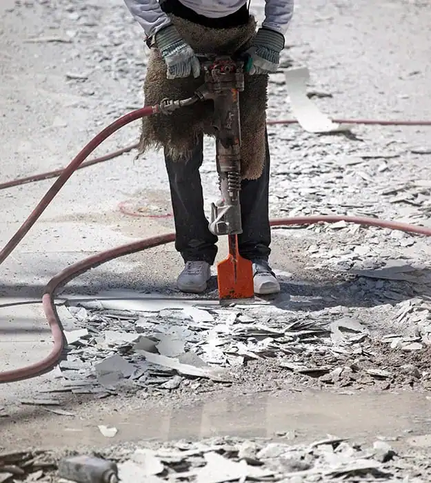 Worker using a jackhammer to break concrete during surface preparation on an industrial job site